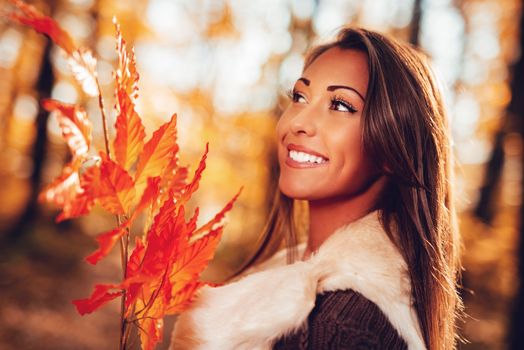 Portrait of a beautiful smiling young woman holding leaf in the nature in autumn.