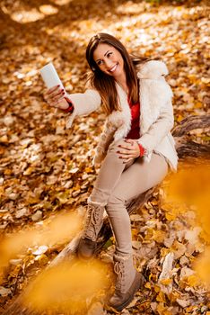 Beautiful smiling girl taking selfie in nature in autumn. 