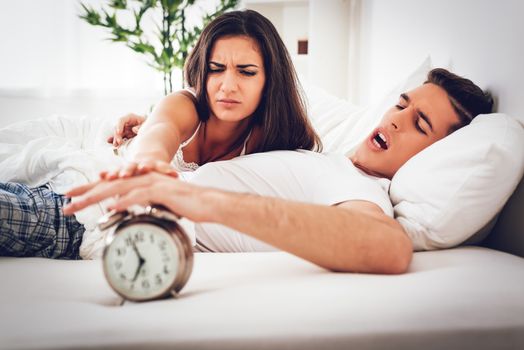 Young anger couple in bed awaken to the ringing of the alarm clock. Selective focus. 