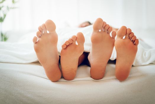 The feet of a heterosexual couple under the covers in bed. Selective Focus, focus on the legs.