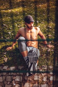 Young serious sportsman doing exercise behind wire at the park.