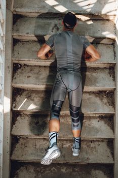 Young urban muscular sportsman doing push-up exercise on the stairs. Rear view. Top view.