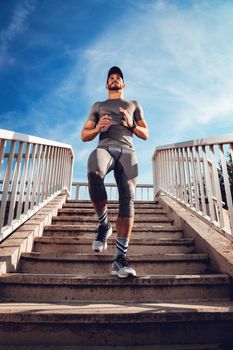 Young muscular sportsman jogging down the stairs at the bridge. 