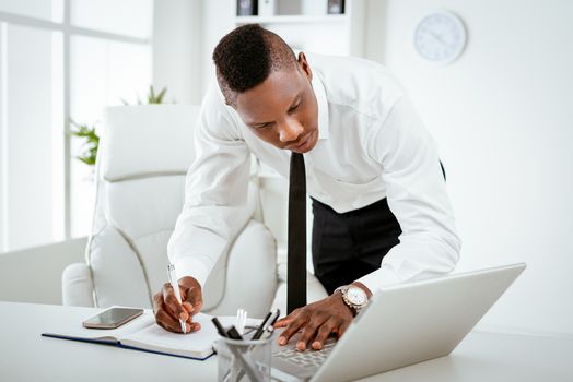 African busy businessman working in the office. He is standing and using laptop. 