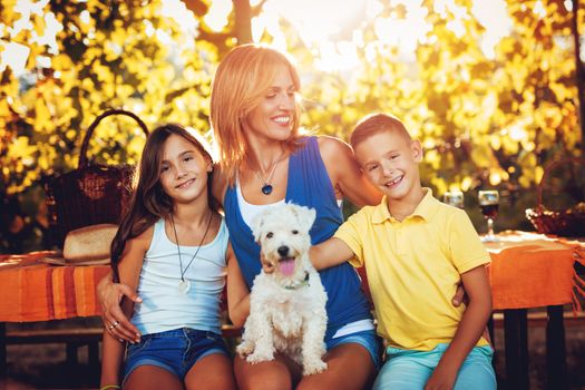 Beautiful smiling mother and her cute children with dog having picnic at a vineyard.