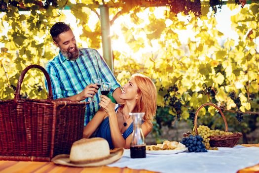 Beautiful smiling couple having picnic and tasting wine at a vineyard.