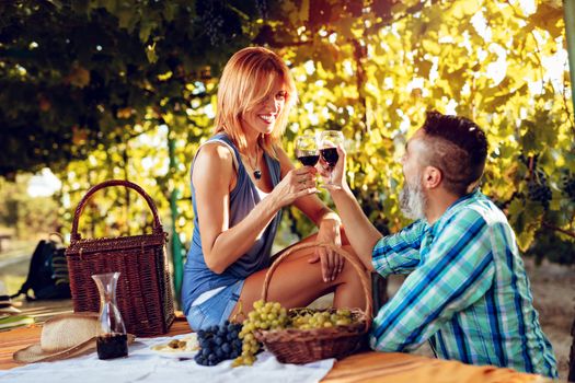 Beautiful smiling couple having picnic and tasting wine at a vineyard.