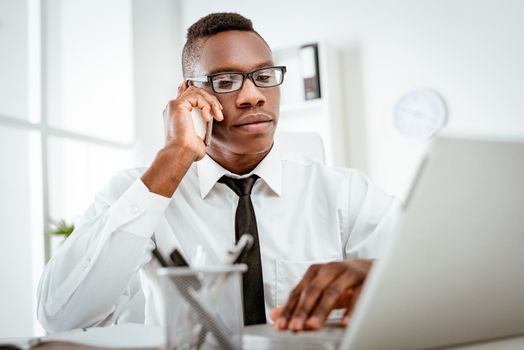 African smiling businessman sitting in the office and using smart phone. 