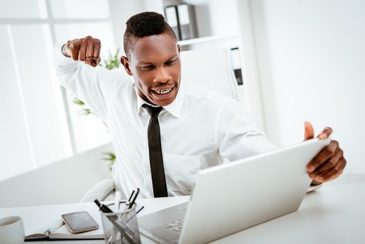 Furious African businessman throws a punch into the laptop in the office.