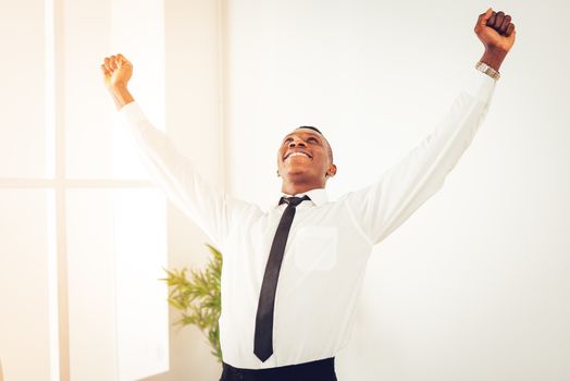 Successful African businessman celebrating success with raised arms in the office.