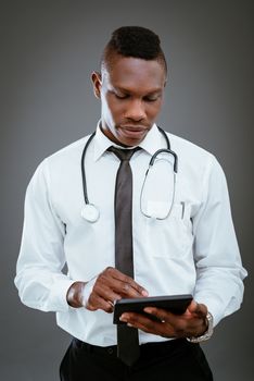 African doctor with stethoscope standing and using digital tablet.