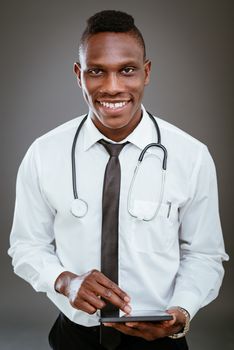 African smiling doctor with stethoscope standing and using digital tablet. Looking at camera.