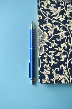 Floral notebook with blue pencils and white and blue background with copy space