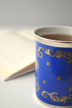 Blue porcelain cup with tea and a book on grey, white and blue background with copy space