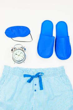 slippers, sleeping mask, alarm clock and pajama top view close-up on a white background