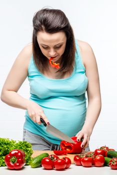 Pregnant woman preparing salad of vegetables in the kitchen