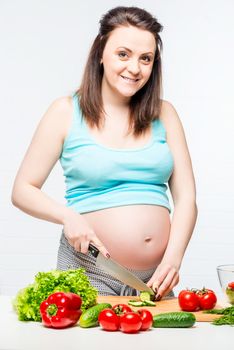 Happy pregnant woman in the kitchen preparing a salad of vegetables