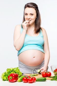 Girl with a big pregnant belly eating a cucumber