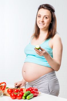 smiling pregnant brunette with fresh cucumber in the kitchen