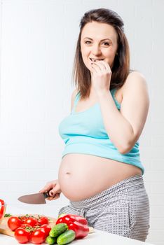 Pregnant girl with big belly in the kitchen eating vegetables