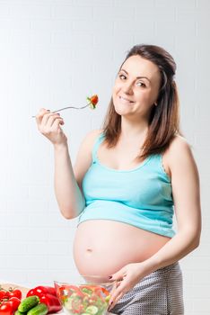 young pregnant woman posing with fresh healthy vegetable salad in the kitchen