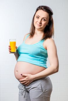 vertical portrait of a pregnant woman with a glass of orange juice