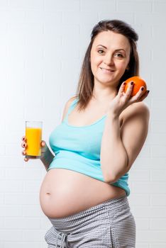 beautiful and happy pregnant woman with orange and a glass of juice on a brick wall background