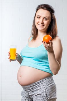 A girl with an orange and a glass of juice is happy, she is pregnant, watches the food