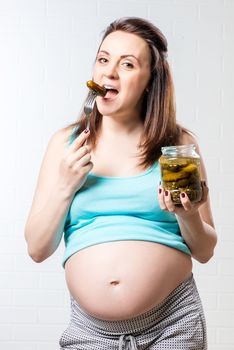 Hungry pregnant woman with a jar of pickled cucumbers against a brick wall background