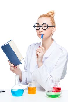 Thoughtful funny chemistry student with a book and test-tubes at the table