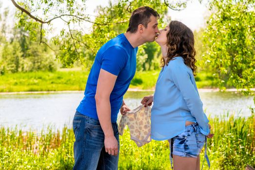 Pregnant woman and her husband kiss in the park near the lake