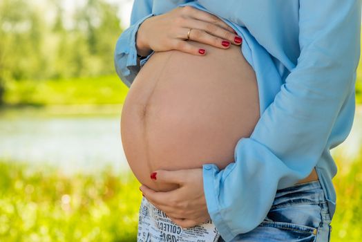 Beautiful big belly of a pregnant woman close-up, shooting in the park