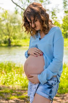 Young pregnant woman hugging her belly with her hands, portrait in the park