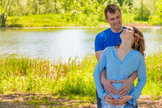 Pregnant woman and her husband in a park near the water hugging