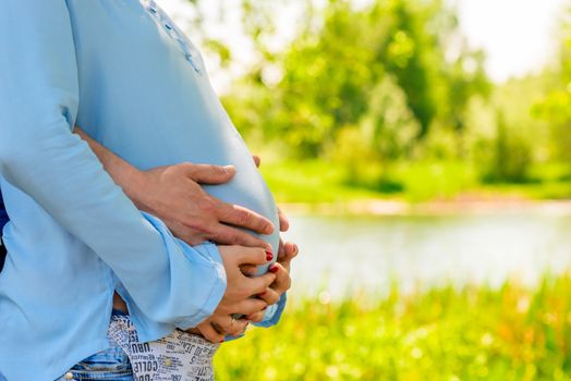 Belly of a pregnant woman embraced by a lake in the park
