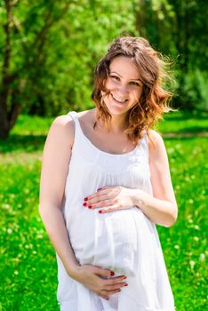 Woman holding her hands belly, waiting for the child on the park background