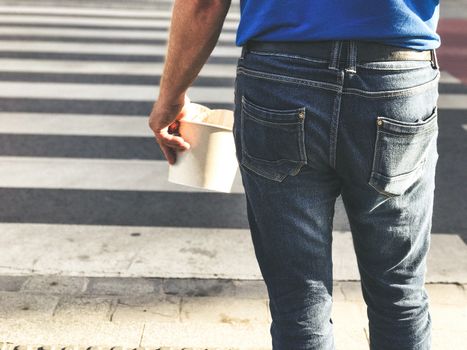 A man holds fast food in his hand and crosses the street