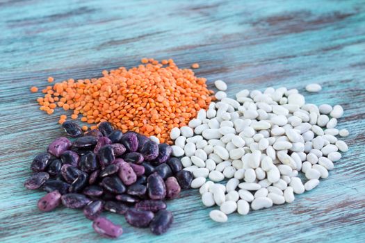 Batch of yellow lentils, white, purple kidney haricot beans scattered on light wooden background
