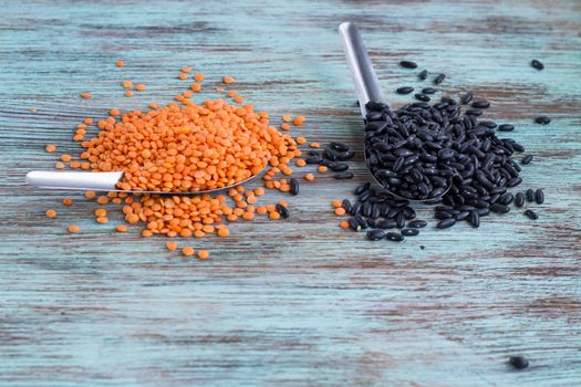 Batch of yellow lentils, black kidney beans scattered on metal spoons on wooden background