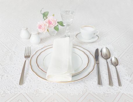 Classically decorated table with white plates, crystal glasses, linen napkin, cutlery and rose flowers on luxurious tablecloths