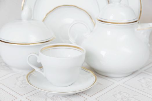 White classic crockery for tea: teapot, cup, serving plate and sugar bowl on a beautiful tablecloths