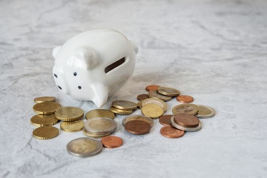 Concept of financial failure: white porcelain piggybank lying on its side surrounded by metal coins