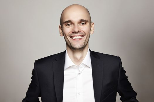 Studio shot of young man looking at the camera. Horizontal format, he is smiling, he is wearing a black jacket.