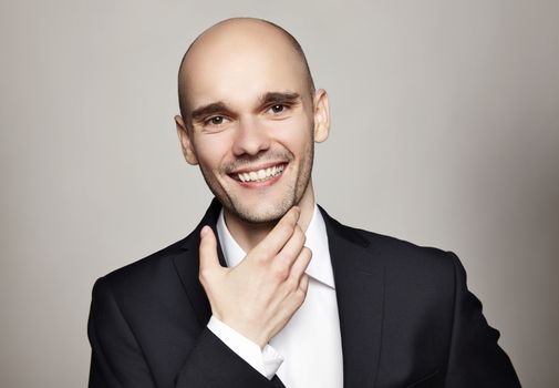 Portrait of smiling man stroking his chin. Headshot on gray background.