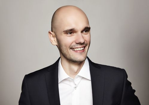 Studio shot of young smiling man. Horizontal format, he is smiling, he is wearing a black jacket.