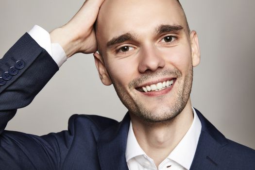 Close-up portrait of a handsome bald man stroking his head. He is smiling. Gray background. Horizontal.