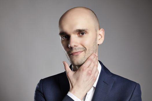 Portrait of a young man stroking his chin. Headshot on gray background.