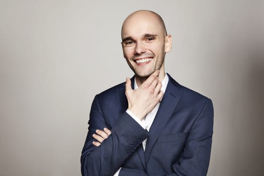 Studio portrait of young cheerful man in blue jacket. He scratches his chin.