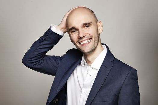 Close-up portrait of a young bald man stroking his head. He is smiling. Gray background. Horizontal.