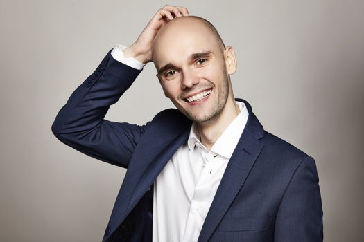 Close-up portrait of a young bald man stroking his head. He is smiling. Gray background. Horizontal.